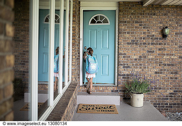 Girl with backpack opening door of house