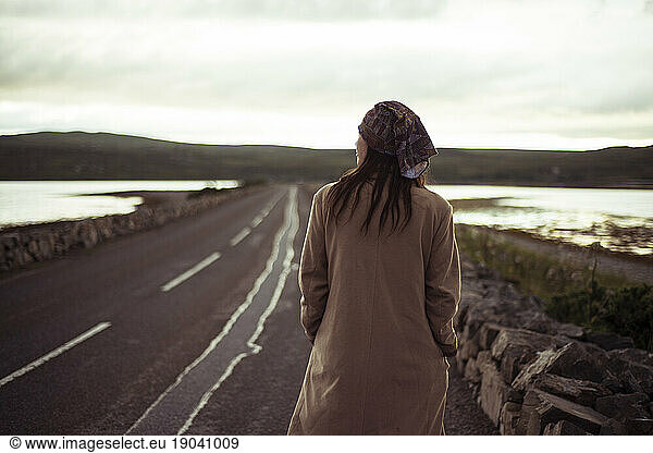 Girl with bandana walks along peaceful road at sunset