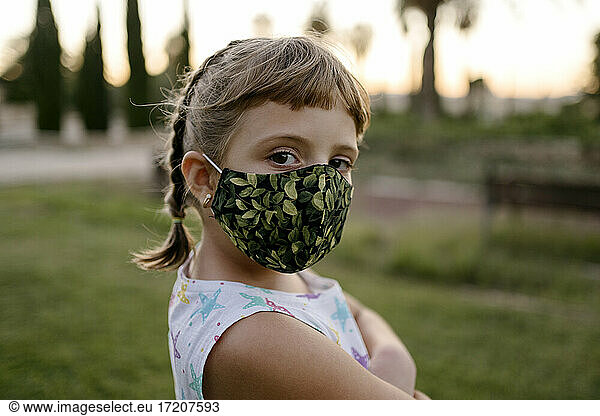 Girl with bangs and protective face mask staring while standing at park