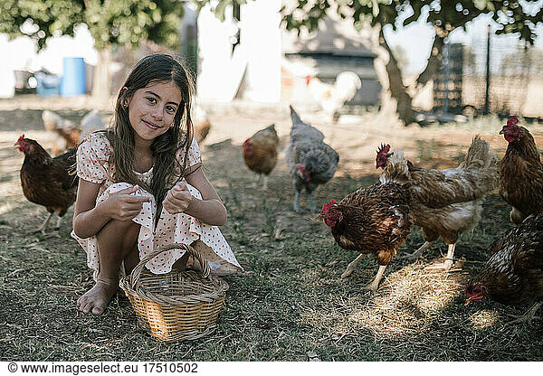 Girl with basket sitting in chicken farm