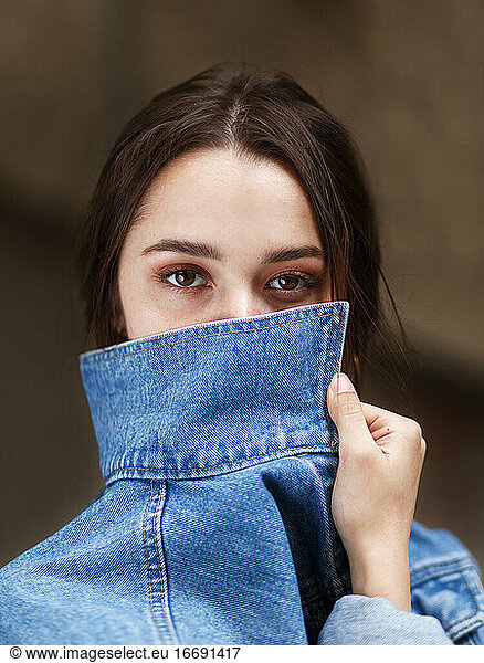 girl with beautiful brown eyes covers her face with a denim collar