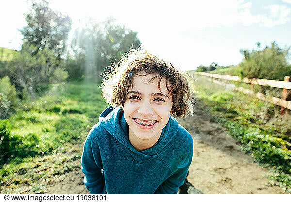 Girl with braces smiles big at camera while outside on a trail