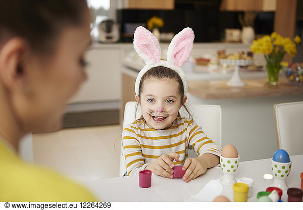 Girl with bunny ears and mother sitting at table with Easter eggs