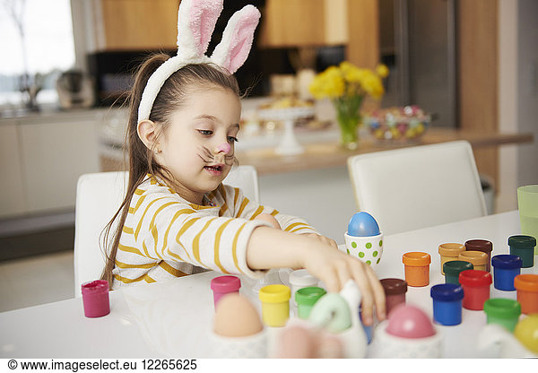 Girl with bunny ears sitting at table painting Easter eggs