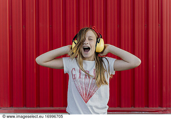 Girl with ear defenders in front of red wall
