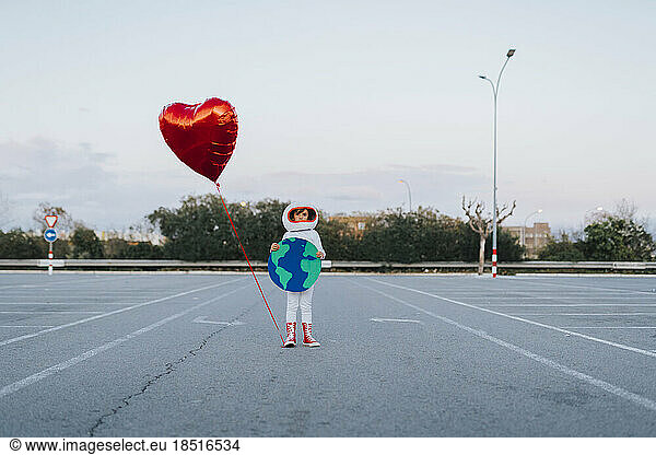 Girl with earth cut out and heart balloon standing in parking lot