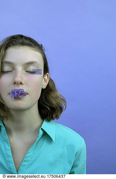 Girl with eyes closed holding flower in mouth against lavender background