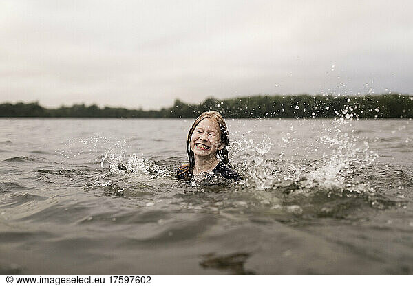 Girl with eyes closed splashing with water in lake