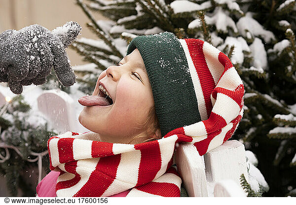 Girl with eyes closed sticking out tongue catching snow in winter