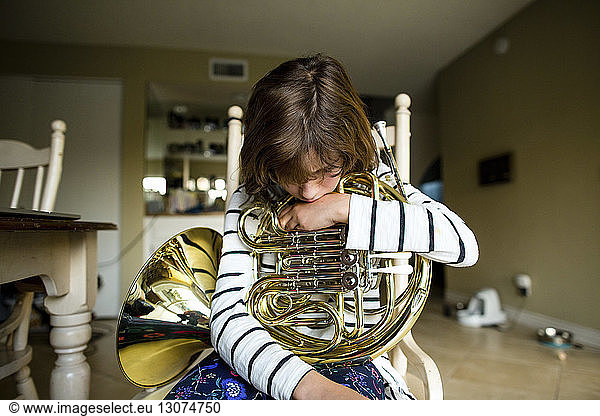 Girl with French horn sitting on chair at home