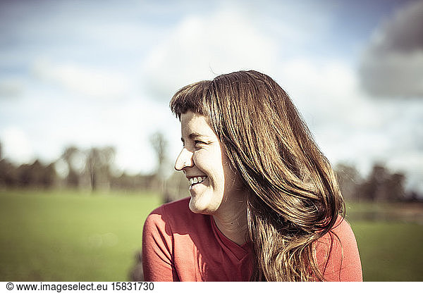 Girl with fringe laughs in sunlight out on green farm land in spring
