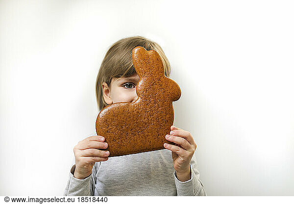 Girl with gingerbread Easter bunny covering face against white background