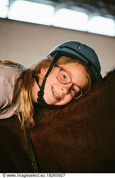 Girl with glasses and braces smiles in riding helmet on horse back