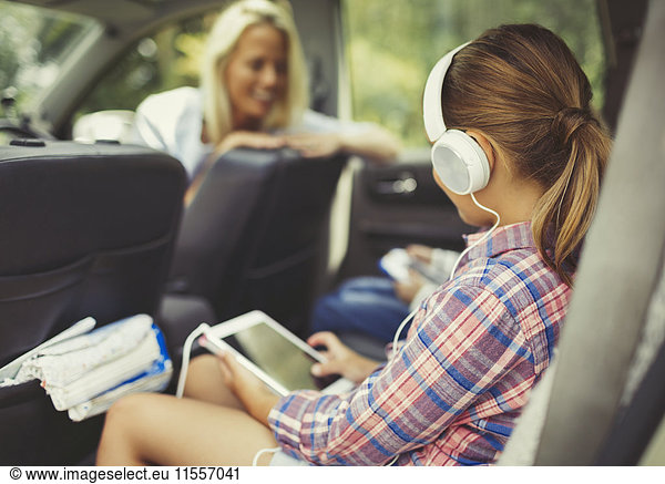 Girl with headphones using digital tablet watching video in back seat of car