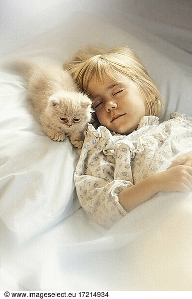 Girl (6-7) with kitten sleeping in bed