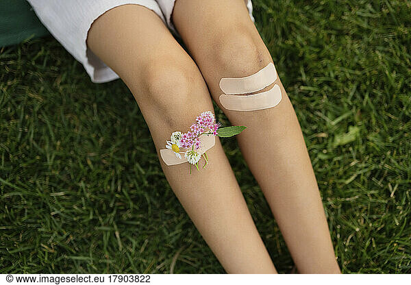 Girl with knees taped by bandage and flowers sitting on grass