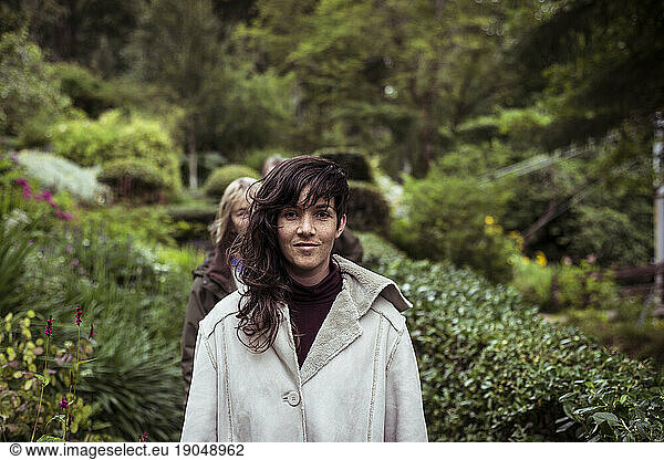 Girl with long wavey hair and warm jacket walks through garden smiling