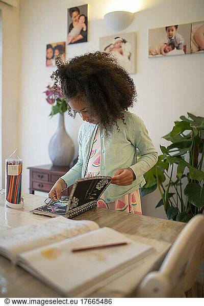 Girl with notebook coloring at dining table