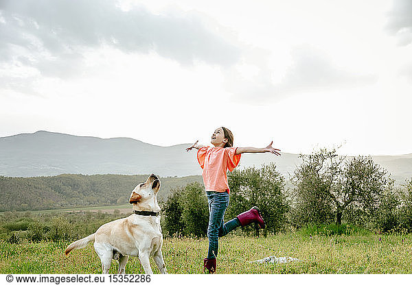 Girl with open arms playing with labrador dog in scenic field landscape  Citta della Pieve  Umbria  Italy