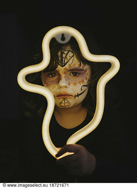 Girl with painted face illuminated by neon in the form of a ghost