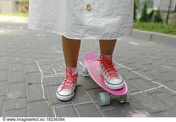 Girl with pink skateboard standing on footpath
