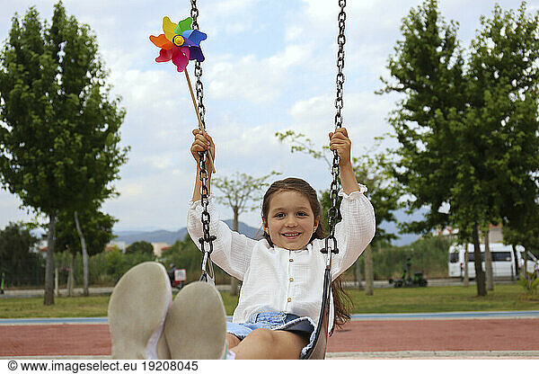 Girl with pinwheel toy swinging on swing
