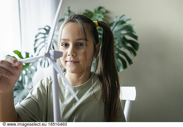 Girl with ponytail touching wind turbine model at home