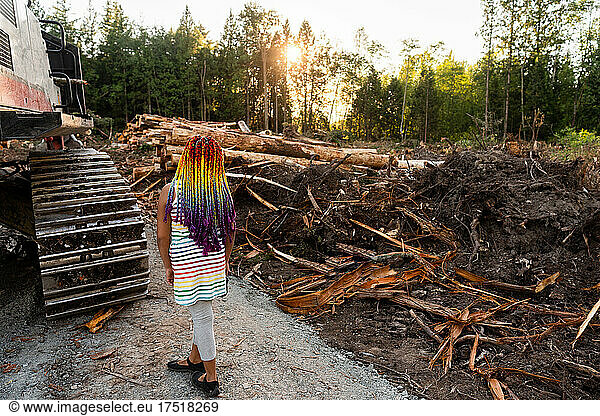 Girl with rainbow braids looks out over logging site