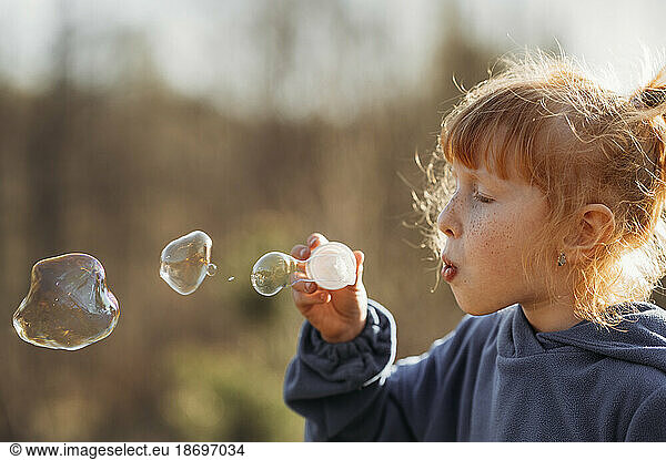 Girl with red hair blowing soap bubbles on sunny day