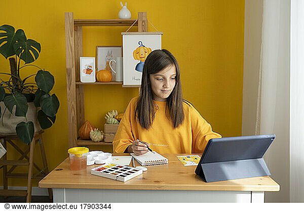 Girl with sketch pad watching online tutorial on tablet PC at home