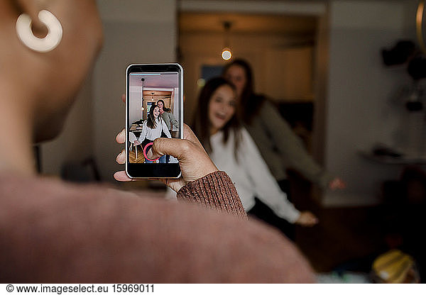 Girl with smart phone filming teenage friends dancing in living room at home
