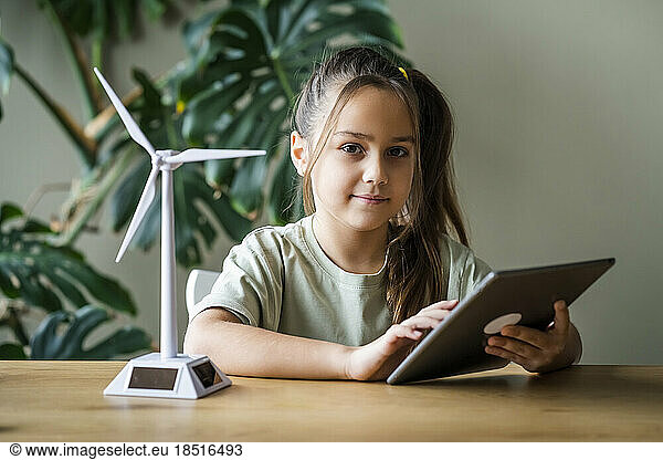 Girl with tablet PC by wind turbine model on table at home