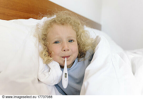 Girl with thermometer in mouth lying on bed at home