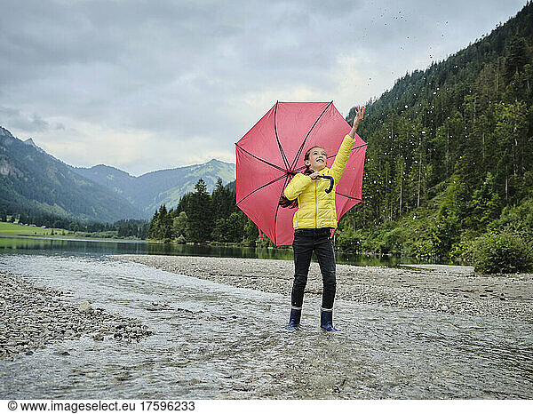 Girl with umbrella splashing water by lakeshore