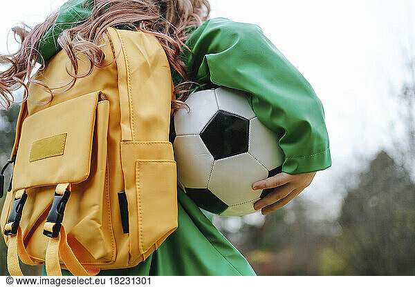 Girl with yellow backpack and soccer ball at park