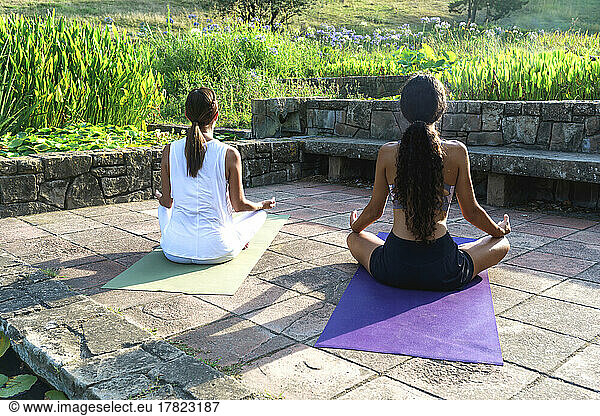 Girl with yoga instructor meditating in park