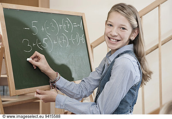 Girl writing arithmetic problem on blackboard