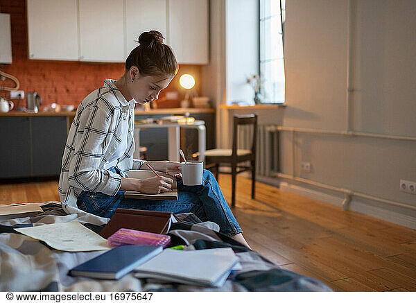 Girl writing notes and drinking hot beverage