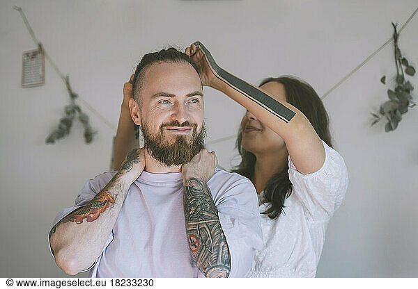 Girlfriend tying hair of smiling hipster boyfriend