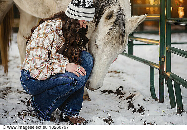 Girling kneeling by white horse in horse pen