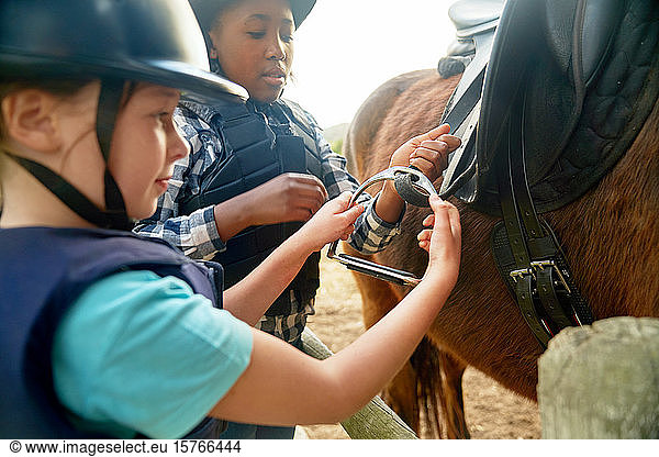 Girls adjust stirrups preparing for horseback riding