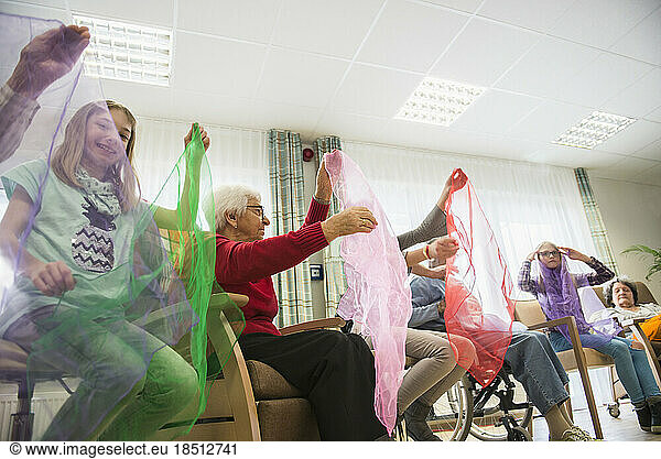Girls and senior women doing gentle sports exercise with cloth in rest home