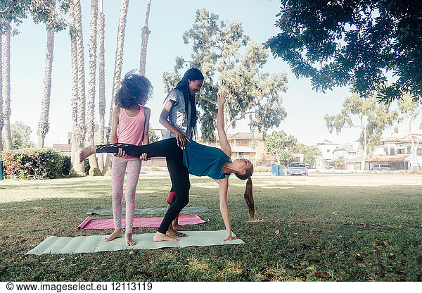 Girls and teenage schoolgirls practicing yoga standing half moon pose on school playing field