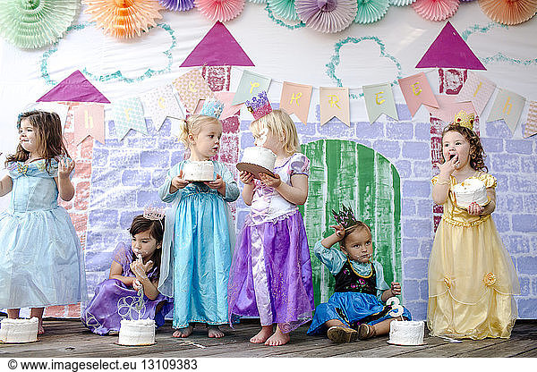 Girls having cakes against castle painting during princess party