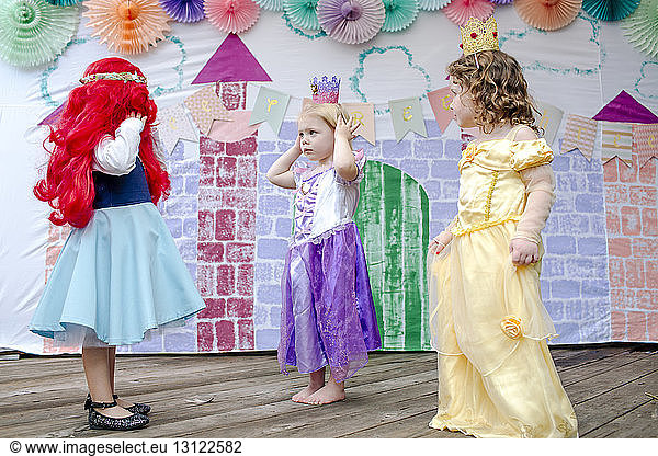 Girls in dress standing against castle painting during princess party