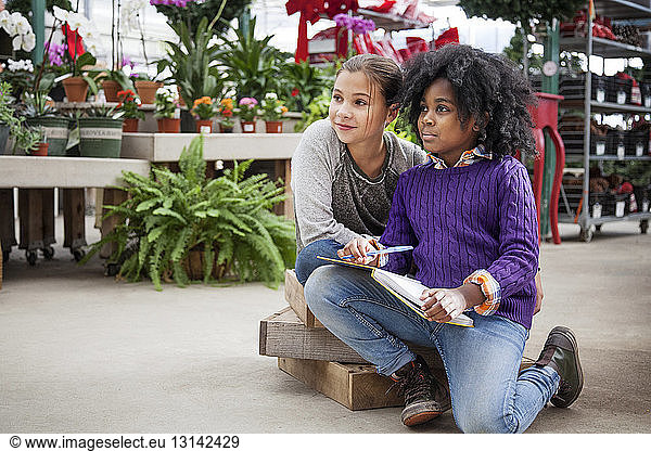 Girls looking away while sitting in plant nursery