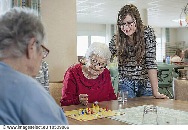 Girls playing ludo board game with senior women in rest home