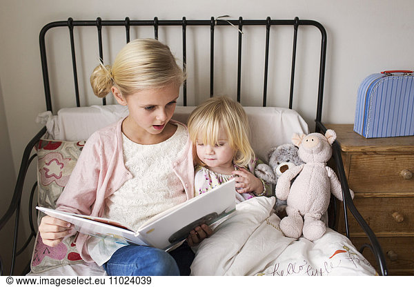 Girls reading book while relaxing on bed at home