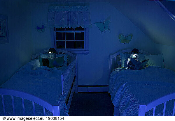 Girls reading in bed by headlamp at night.