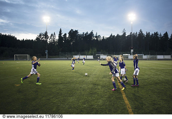 Girls running on soccer field against sky